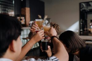 Friends raise glasses in a celebratory toast at a bar setting. Indoor lighting and social atmosphere.